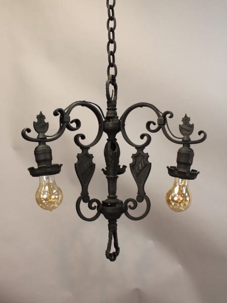 The 15646. Spanish Revival 1920's Chandelier With Crest Motif, with ornate iron scrolls and three exposed light bulbs, hanging from a chain against a gray background.