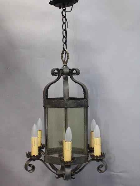An antique 15775. 1920's chandelier with four candle-shaped bulbs and frosted glass panels, suspended by a chain against a grey background.
