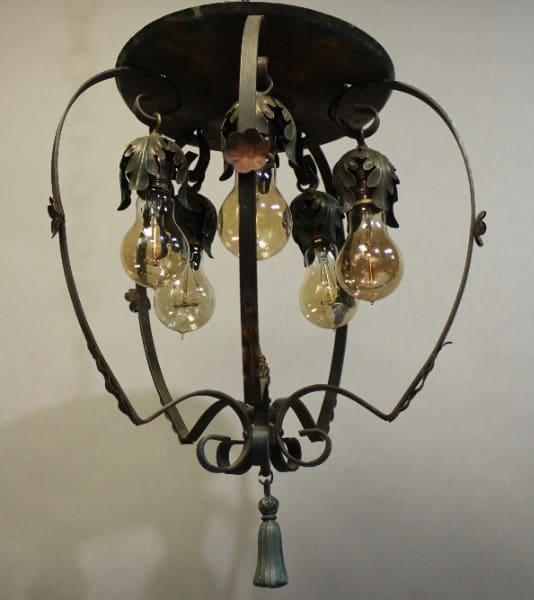 15920. 1920's Spanish Revival Chandlier With Five Lights with four exposed bulbs hanging from scrolled iron arms, decorated with metallic leaves, against a light background.