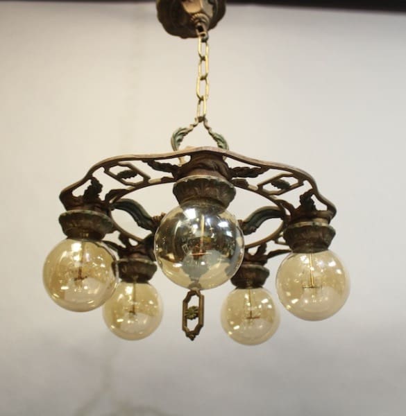 15929. 1920's Downlight Chandelier With Leaf Motif with ornate bronze frame and five hanging spherical glass bulbs, illuminated and suspended from a ceiling chain.