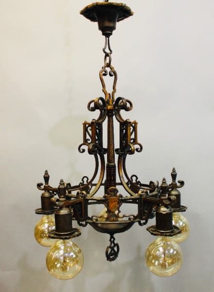 15932. Spanish Revival 1920's chandelier with ornamental details and six illuminated glass globes, suspended from a ceiling mount.