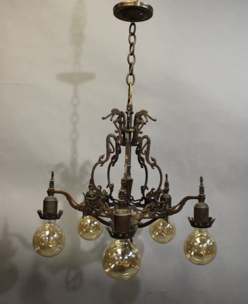 15955. 1920's Chandelier With Original Polychrome Finish with five glowing light bulbs, suspended from a chain, featuring ornate metalwork and intricate designs.