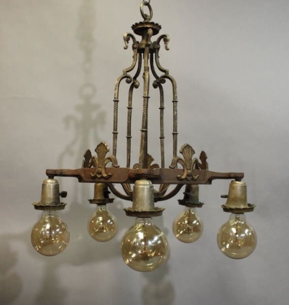15957. Tudor Style 1920's Chandelier with ornamental designs and five hanging glass bulbs, suspended in a room with a gray background.