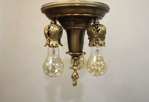 15964. 1920's Brass Ceiling Mount With Acanthus Leafs chandelier with three hanging clear glass light bulbs, featuring ornamental eagle designs.