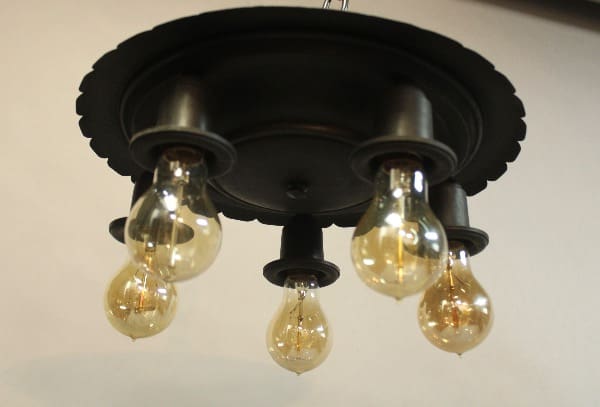 A black 15970. Circa 1920's Iron Ceiling Mount with five glowing, teardrop-shaped bulbs suspended underneath.