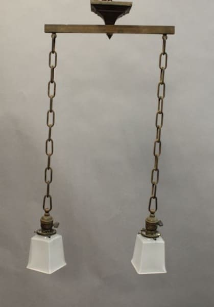 Vintage pendant light fixture with two white glass shades suspended by metal chains against a gray background.