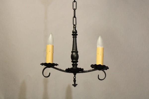 A hanging 16207. Small Spanish Revival 1920's Pendant with a dark metallic finish and two candle-like bulbs against a plain light background.