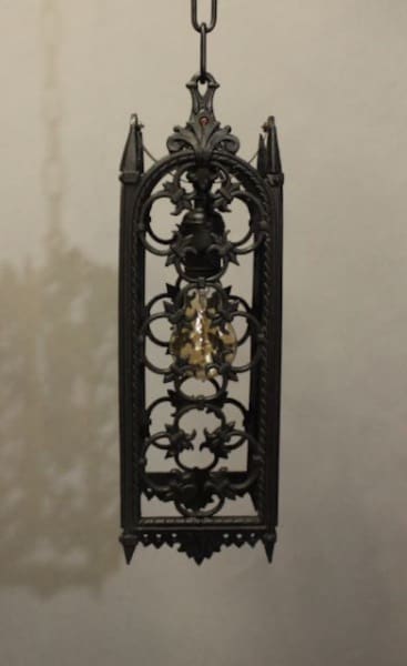 An ornate 16211. Spanish Revival Pendant With Clover Motif with intricate metalwork and a visible light bulb, suspended against a softly illuminated background.