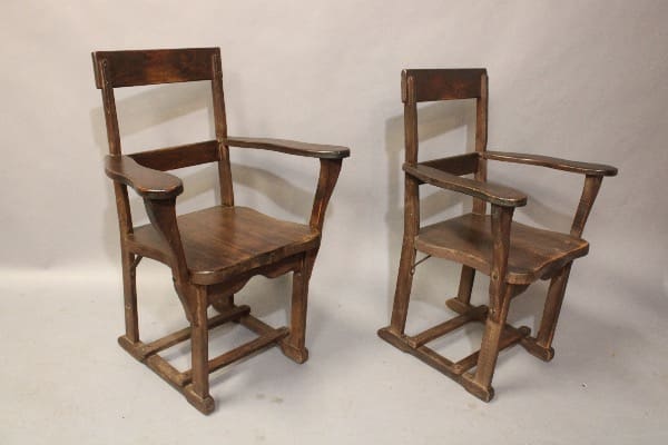 Two antique wooden chairs with armrests on a plain background. the 16228. Pair Of Signed Monterey Armchairs are sturdy with a simple design, showing signs of wear.