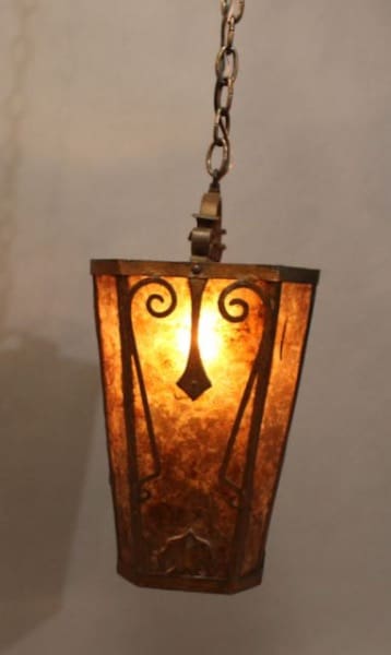 A hanging pendant light with a 16326. Large Scale 1920's Pendant With Mica frame and amber-colored glass panels, lit from within, casting a warm glow.