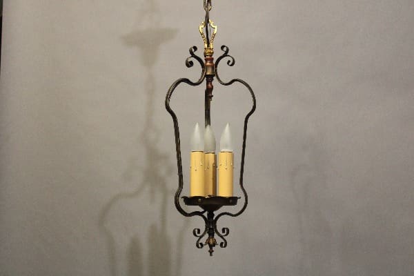 Spanish Revival Three Light Pendant with four candle-shaped lights, hanging from a chain against a gray wall.