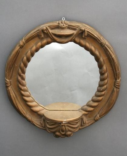 341. Small Round Mirror with an ornate wooden frame, featuring carved ribbons and floral motifs, hung on a gray wall.
