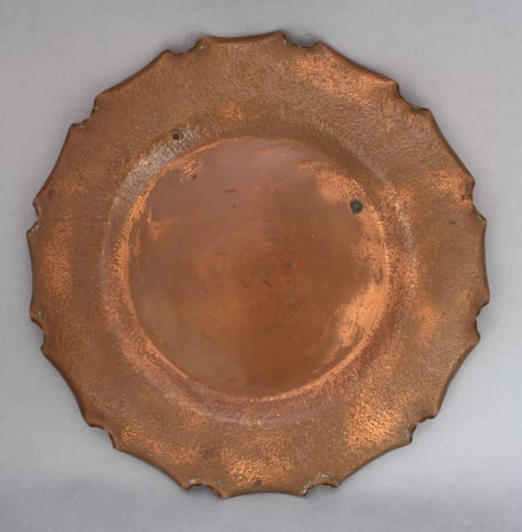 An old, round 9321. Arts & Crafts Blue Hills Crafts Hammered Copper Plate with a scalloped edge and tarnished surface, showing signs of wear and rust spots.