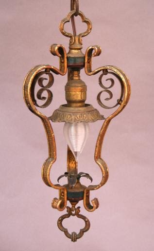 960. Spanish Revival hall pendant with ornate metal scrollwork and a single frosted glass bulb, suspended against a pink background.