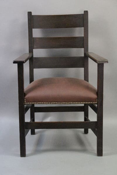 A 10273. Ladder Back Arts And Crafts Armchair with a dark finish and a brown upholstered seat, accented with small decorative nails along the edges.