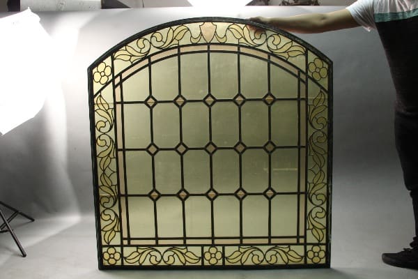 A person holding a 11321. 1 Of 2 Arched Stained Glass Window in a photography studio.