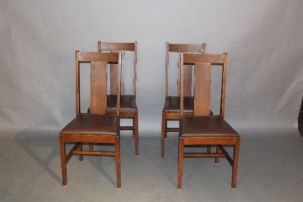 Four 11692. Set Of Four Arts And Crafts Side Chairs with brown leather seats arranged in two pairs facing each other, against a grey backdrop.