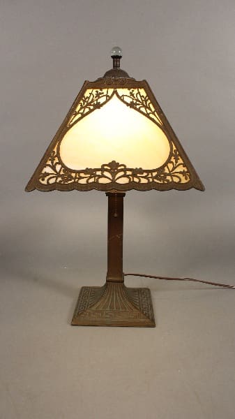 11774. Turn Of The Century Table Lamp With Slag Glass with an ornate bronze base and a triangular stained glass shade, illuminated, against a neutral background.