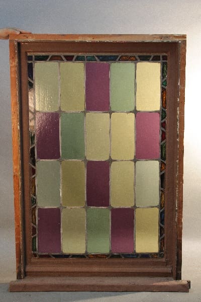11865. Spanish Revival 1920's Stained Glass Panel with a geometric pattern of various muted colors, encased in a dark wooden frame.