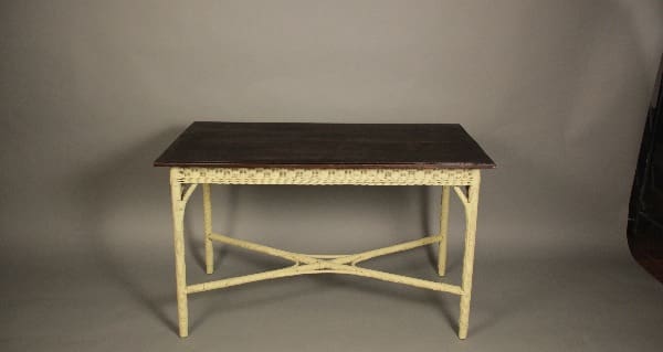 A rectangular wooden table with a dark brown top and a distressed white base featuring x-shaped legs, set against a gray backdrop.
