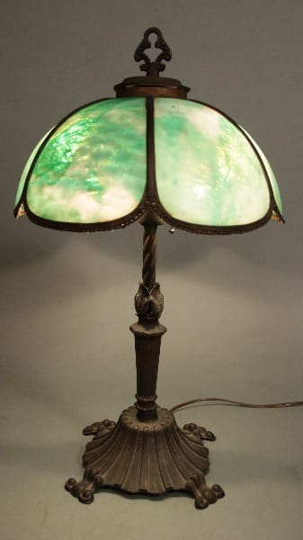 12105. Turn Of The Century Table Lamp with a green tiffany glass shade and ornate bronze base featuring floral detail.
