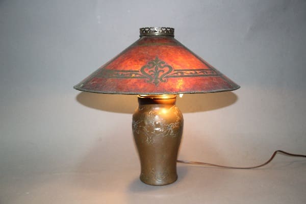 12323. Copper Turn Of The Century Lamp with ornate metal base and stained glass shade featuring a floral design, illuminated on a plain background.