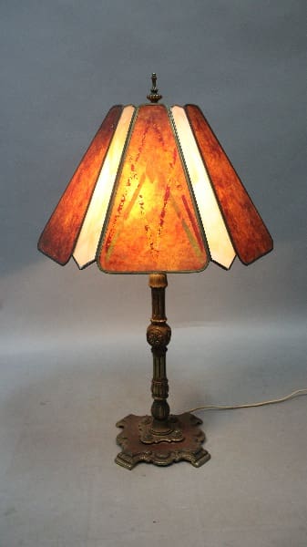 12560. 1920's Table Lamp With Glass Shade with a stained glass shade in orange and white, standing on an ornate bronze base, illuminated.
