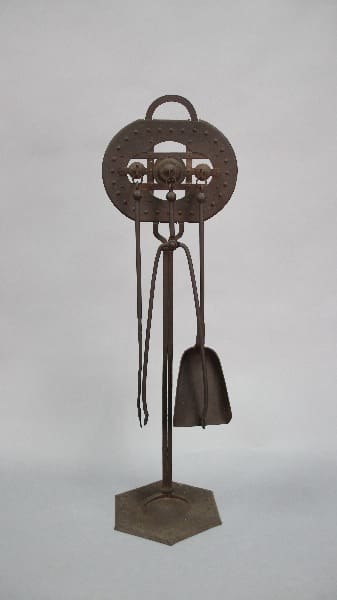 A vintage hat stand made of metal with a circular design and hooks, featuring the 12701. Turn of The Century Hand Hammered Tool Set hanging on one side.