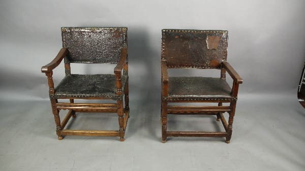 Two antique wooden armchairs with worn upholstery.
