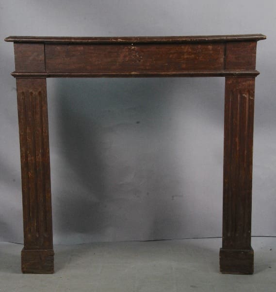 Antique 13199. Turn Of The Century Mantel Front with a simple, rectangular top and thick, square legs, showing signs of wear and age, against a gray backdrop.