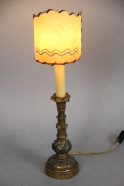 13325. Spanish Revival Carved Wood Small Lamp with an illuminated cream lampshade featuring a scalloped edge and dark wavy lines, set against a plain gray background.