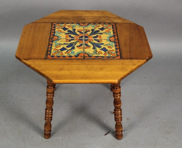 An octagonal wooden table with turned legs and a colorful ceramic tile inlay in the center.