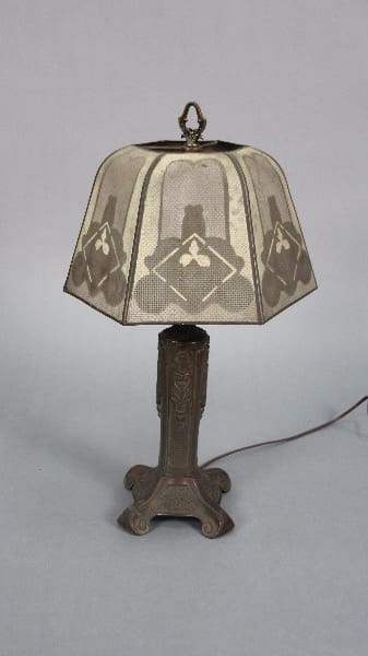 Vintage table lamp with a decorative metal base and a stained glass shade featuring geometric patterns, set against a plain background. 13395. Spanish Revival 1920's Table Lamp With Metal Shade