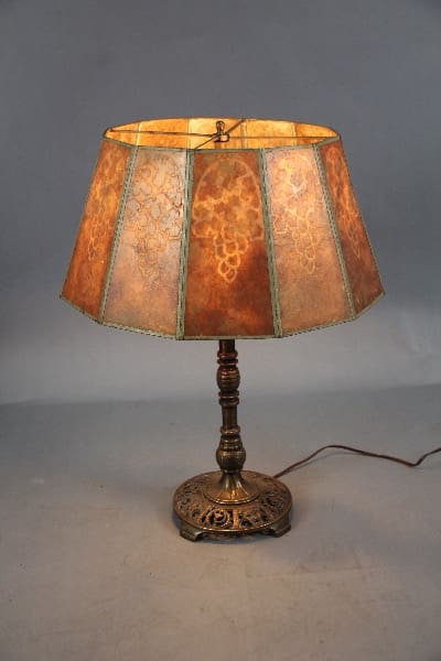 Spanish Revival table lamp with a decorative, patterned mica shade and an ornate bronze base, illuminated and set against a gray background.