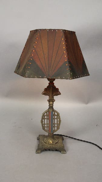 A 13449. 1920's All Original Spanish Revival table lamp with a decorative metal base and a cone-shaped shade with small perforations, emitting a soft light.