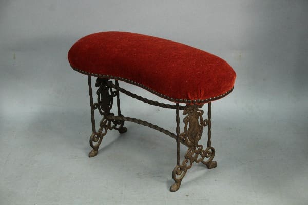 Vintage red upholstered bench with ornate legs.