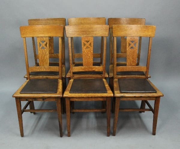 A 13883. set of six vintage wooden chairs with leather seats and decorative x-shaped backrest designs, arranged in two rows on a plain backdrop.