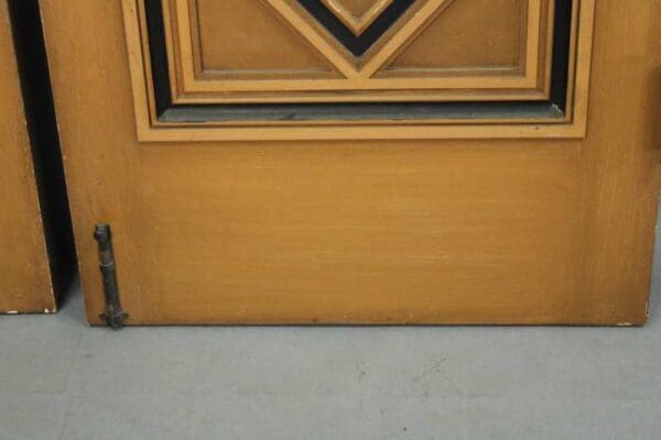 A close-up of a 14016. Pair Of Fantastic Double Doors From 1920's Spanish House, with a geometric glass panel and metal hinge, set against a gray floor.