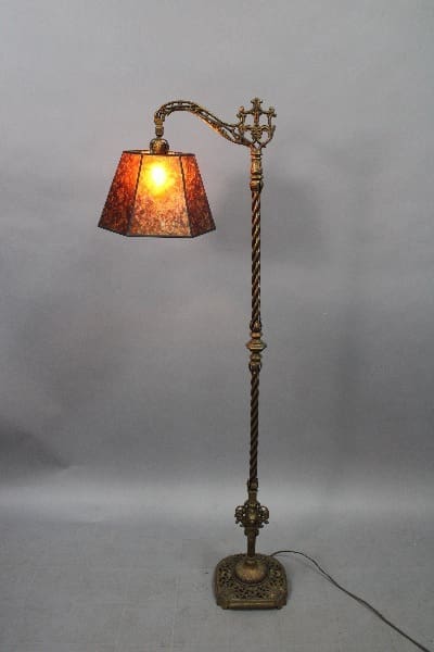 Spanish Revival 1920's bridge lamp with a twisted metal post, ornate details, and a lit stained glass shade against a gray background.
