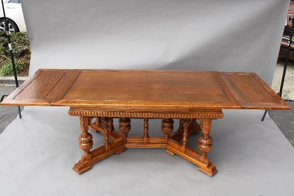Antique 14141. 1920's Spanish Revival dining table with extension and ornate legs, set against a plain white backdrop on a driveway.