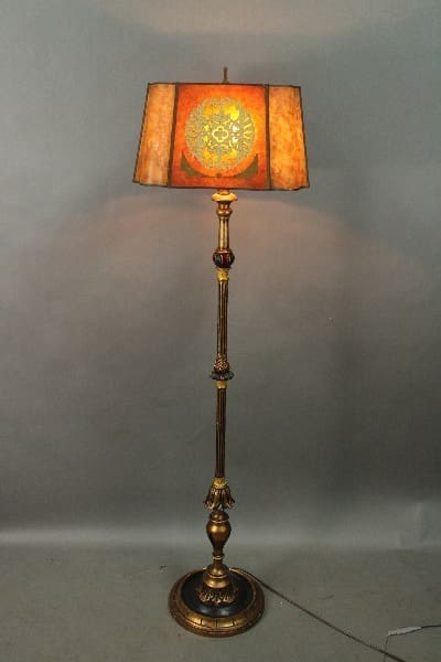 An 14304. Spanish Revival 1920's With Polychrome Base And Original Mica shade with a decorative metal base and an ornate, orange-toned lampshade, illuminated, against a gray background.