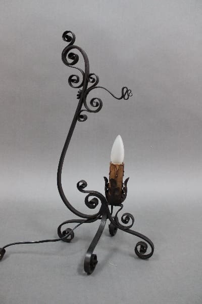 An ornate 14344. Spanish Revival wrought iron candle holder with a single white candle, set against a gradient gray background.