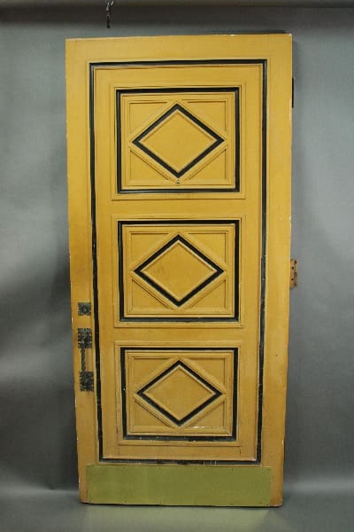 A 14493. Original 1920's front door with original hardware, featuring four diamond-shaped panels, painted yellow, standing against a grey background.