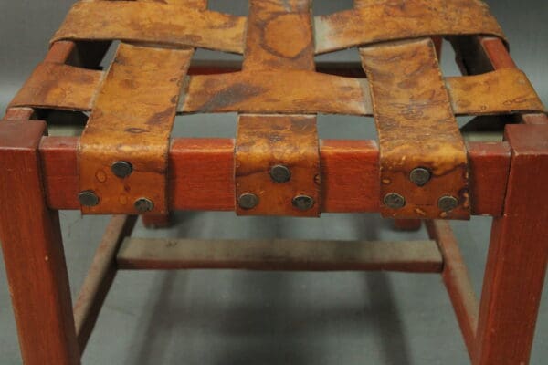 Wooden stool with leather straps and rivets.