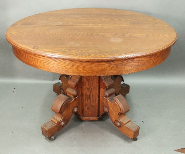 A 14690. 1910 Dining Room Table Oak with a detailed carved pedestal base and multiple feet, positioned on a plain grey surface.