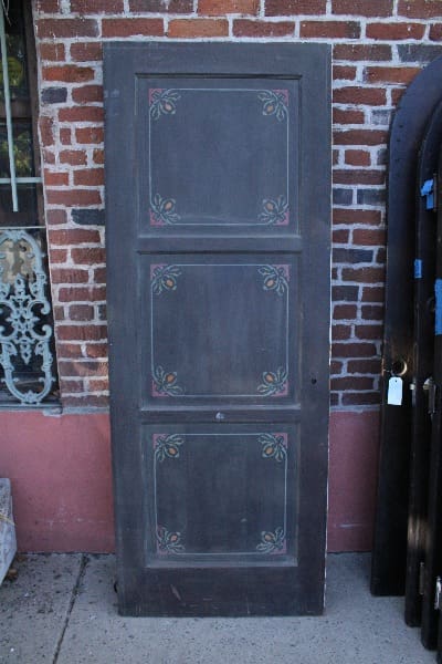 An upright 14776. Spanish Revival 1920's door with four panels, each adorned with a simple floral design, leaning against a red brick wall.