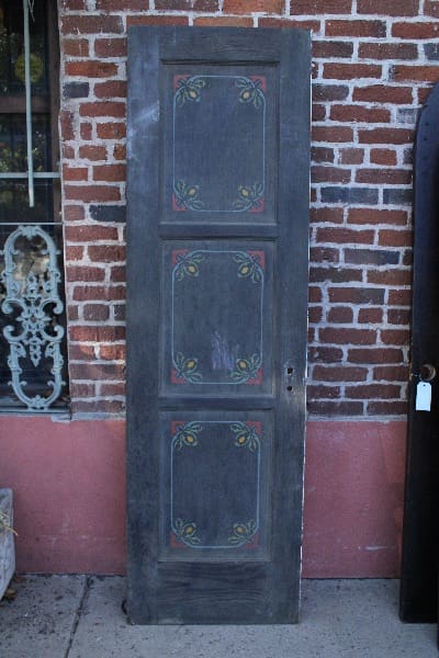 A 14777. Spanish Revival Painted Door with three panels, each featuring decorative floral carvings, standing against a red brick wall.
