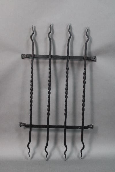 14816. 1 of 2 Iron Grill From 1920's House fragment with twisted and curvy vertical bars, mounted on a gray background.