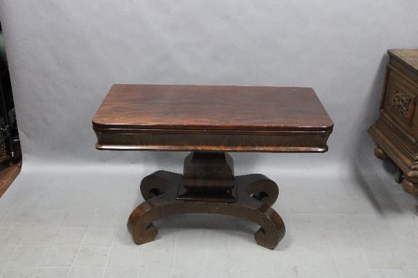A 14846. Game Table Early 20th Century with a rectangular top and curved legs, set against a plain grey background in a room with another furniture piece partially visible to the right.