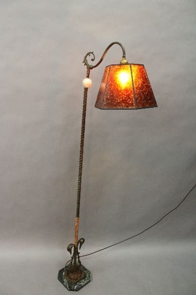 14855. Spanish Revival Floor Bridge Lamp With Movable Shade with a twisted metal stand and a square, stained-glass shade emitting a warm glow, set against a plain gray background.